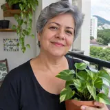 Mulher de cabelos grisalhos curtos segurando um vaso de jiboia na varanda