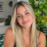 Mulher loira sorrindo em uma sala com plantas ao fundo
